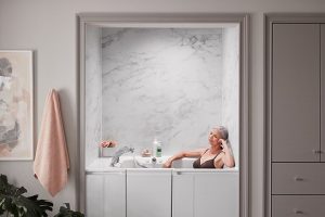 Senior woman relaxing in a KOHLER walk-in tub with KOHLER LuxStone bath walls installed and a bath towel hanging outside of the tub.