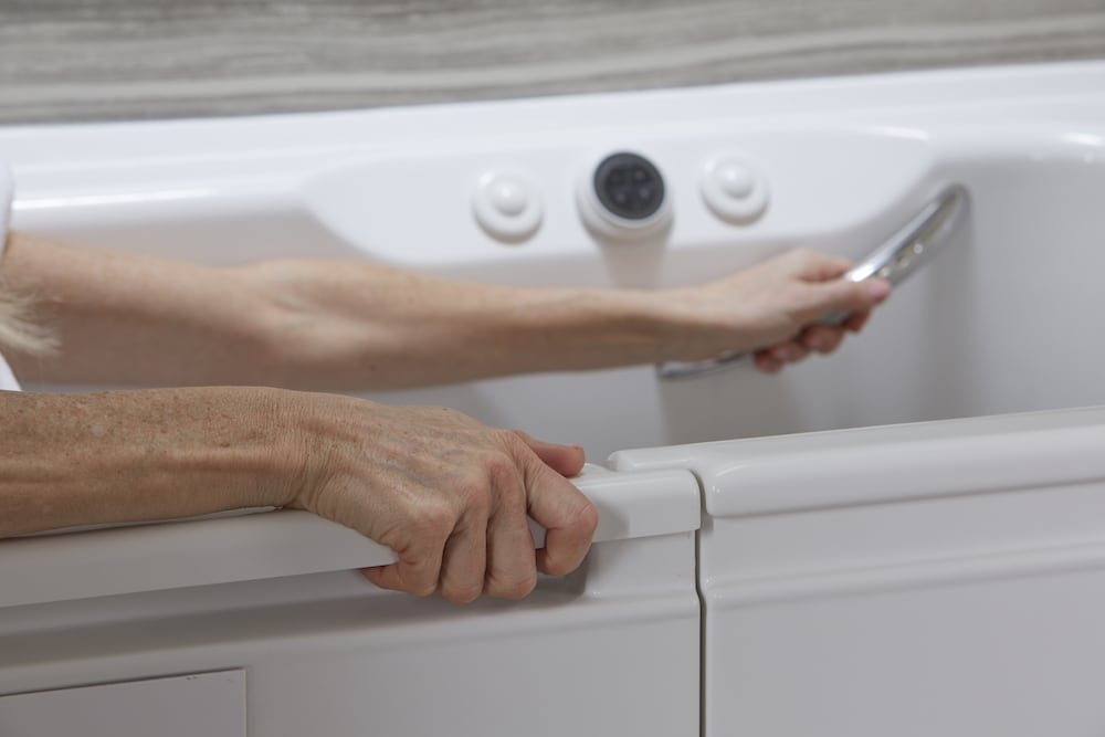 Woman uses handrail in walk-in bath.