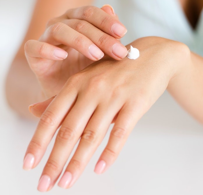 A woman applying body lotion to the back of her left hand using her right middle finger