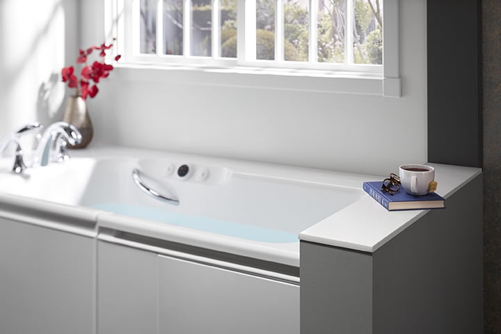 White tub against bathroom wall with book and flowers on the tub ledge