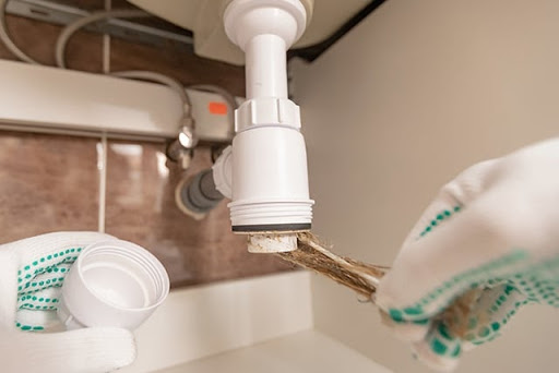 Person with gloves removing clog from pipes