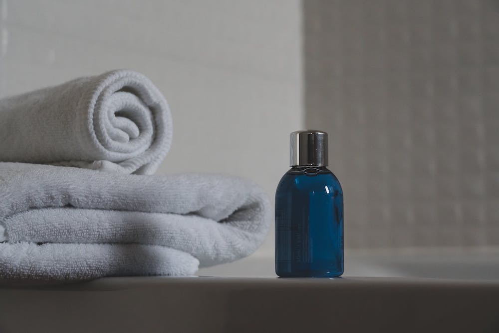 Fragrance bottle on ledge of bathtub beside stock of towels