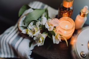 Bathroom counter with flowers, a serum, bath towel, and lit candle.