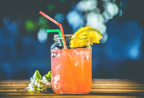 Orange drink with a lemon slice and two bendy straws sitting on top of a wooden table.