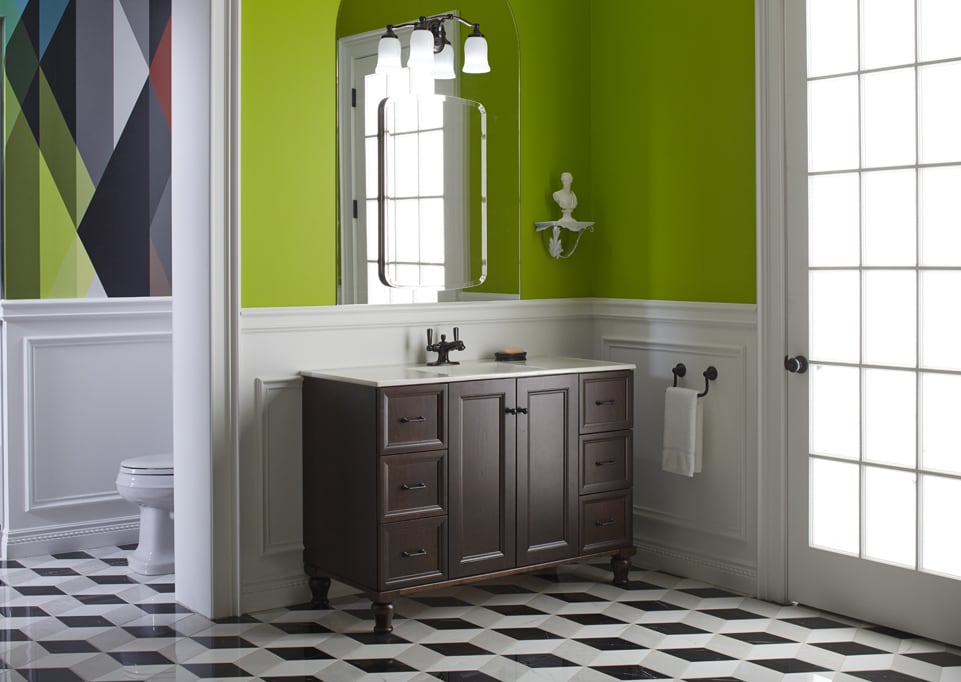 Green bathroom with retro flooring and a wall separating the vanity sink area and the toilet