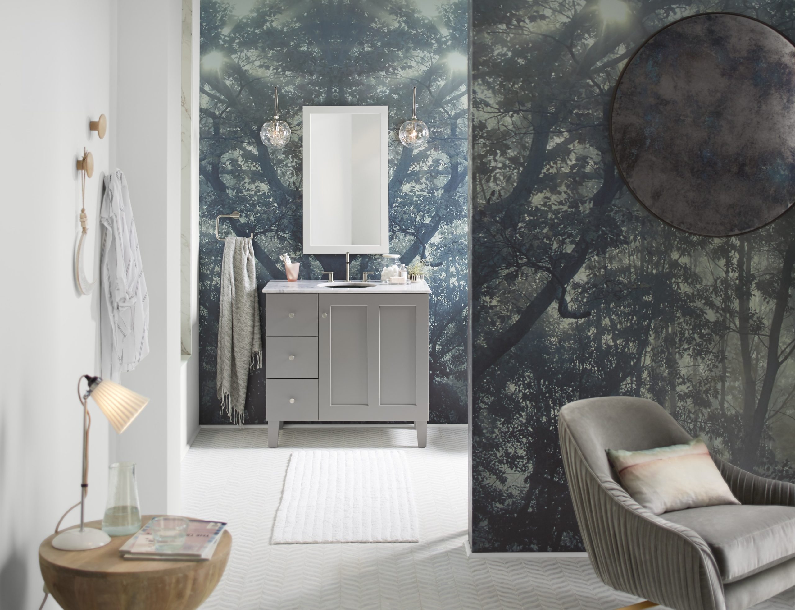 large bathroom with herringbone tile floors and blue wallpaper as well as a gray single vanity with a mirror and two scones on either side of the mirror