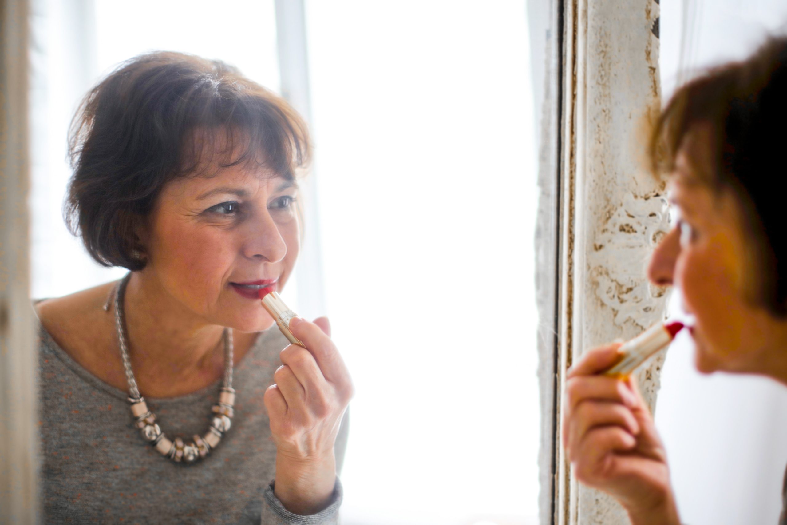 senior woman applying red lipstick in a mirror