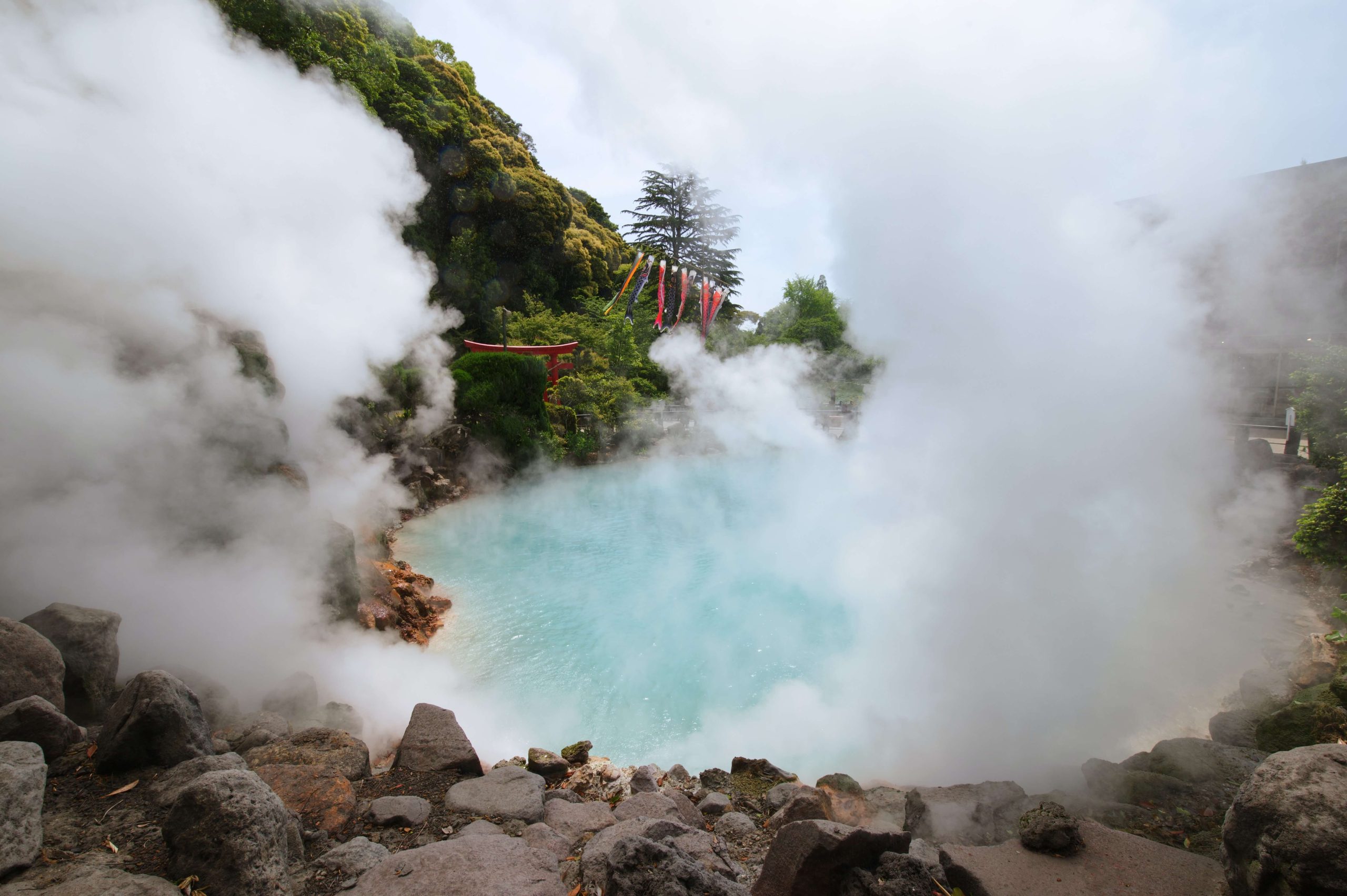 Japanese onsen shown with clear blue water and steam coming up onto the rocks