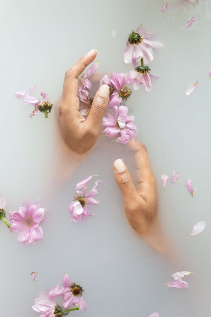 Hands in milky bath water holding flower petals
