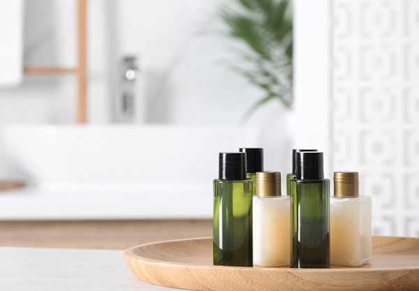 Wooden tray with mini bottles of cosmetic products on white table in bathroom.