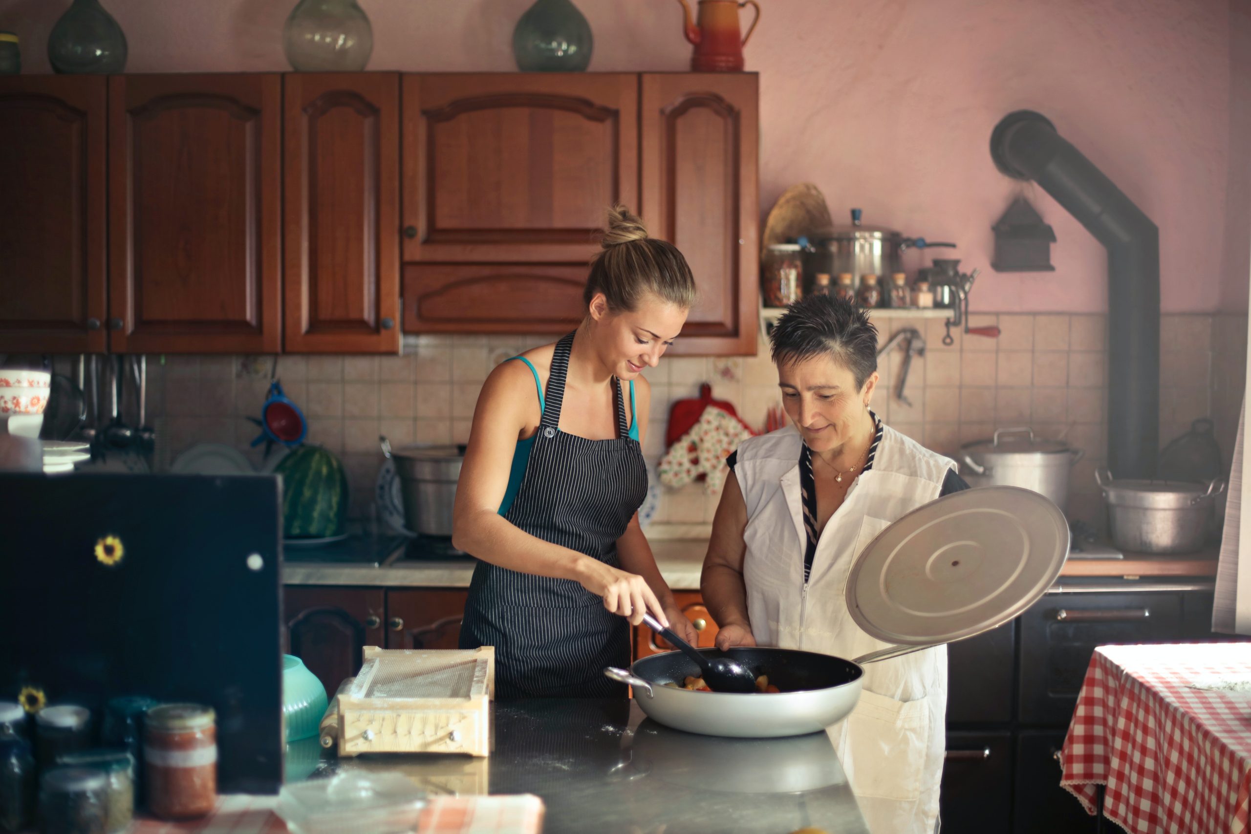 Young woman wearing an apron stirring a large pot and standing in the kitchen with an older woman.