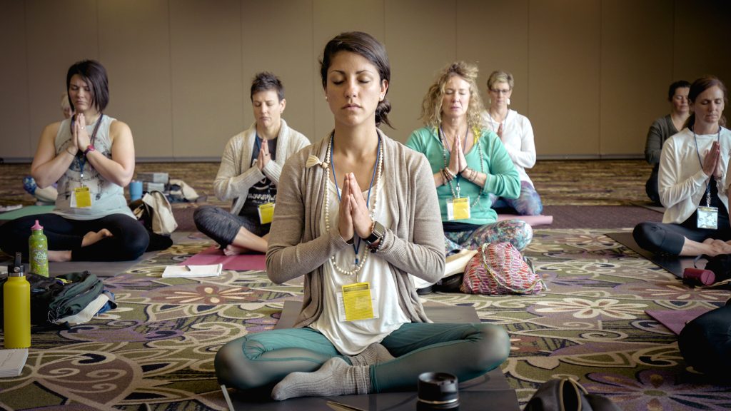 Group of women sitting on the floor meditating with their hands at heart's center.