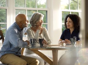 three people sitting at a circular dining table drinking coffee with the youngest of the three talking and using her hands