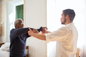 In-home nurse in a white button down shirt holding an older man's arms up by his wrists