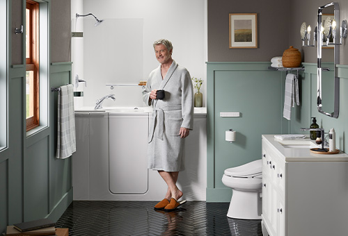 Man drinking coffee in front of the KOHLER Walk-In Bath featuring the Shower Package