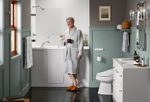 Man drinking coffee in front of the KOHLER Walk-In Bath featuring the Shower Package