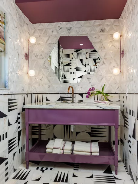 Small powder room with a purple vanity with a hexagonal mirror and two sconces on each side of the mirror